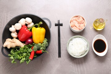 Wok, chopsticks and different products on grey textured table, flat lay