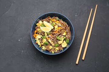 Stir-fry. Delicious cooked noodles with chicken and vegetables in bowl served on gray textured table, flat lay