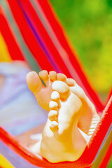 Fototapety  Close up young beautiful girl sleeping in a hammock with bare feet, relaxing and enjoying a lovely sunny summer day. Safety and happy childhood and leisure concept. Vertical image.