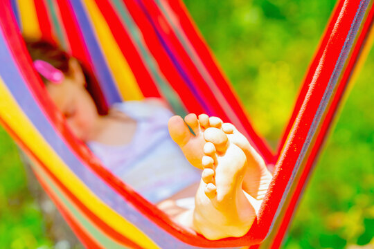 Young beautiful girl sleeping in a hammock with bare feet, relaxing and enjoying a lovely sunny summer day. Green vegetation in background. Safety and happy childhood concept