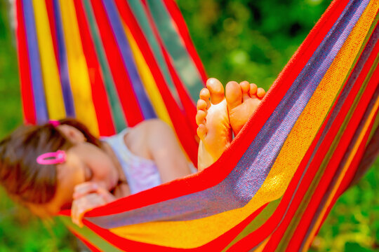 Young beautiful girl sleeping in a hammock with bare feet, relaxing and enjoying a lovely sunny summer day. Green vegetation in background. Selective focus on bare feet