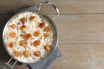 Delicious scallop pasta in pan on wooden table, top view. Space for text