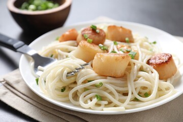 Delicious scallop pasta with green onion served on grey table, closeup