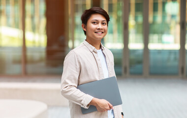 Young asian businessman walking by downtown with laptop