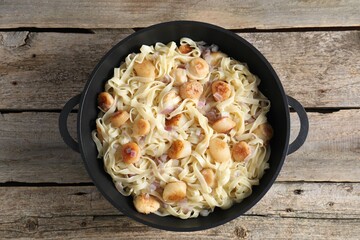 Delicious scallop pasta with onion in pan on wooden table, top view