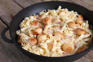 Delicious scallop pasta with onion in pan on wooden table, closeup