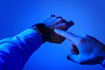 Young man points to digital display of smartwatch, cropped shot