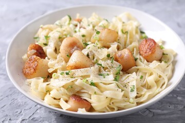 Delicious scallop pasta with spices in bowl on gray textured table, closeup