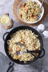 Delicious scallop pasta with spices in bowl on gray textured table, flat lay