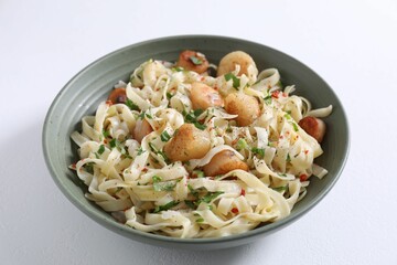 Delicious scallop pasta with spices in bowl on white table, closeup