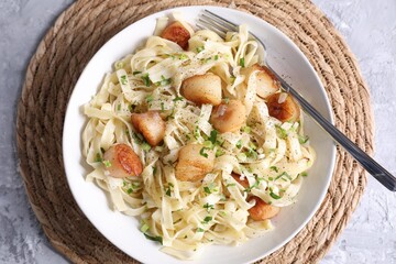 Delicious scallop pasta with spices in bowl on gray textured table, top view