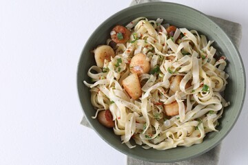 Delicious scallop pasta with spices in bowl on white table, top view. Space for text