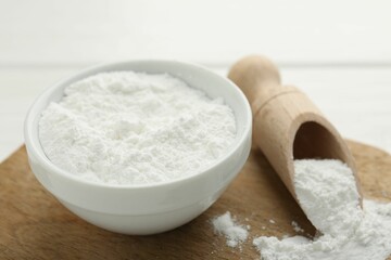 Fototapeta na wymiar Baking powder in bowl and scoop on white wooden table, closeup