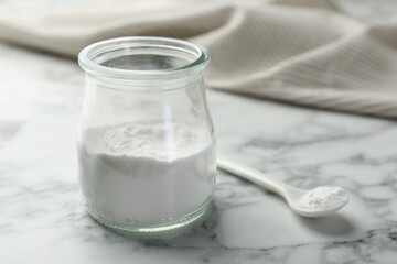 Baking powder in jar and spoon on white marble table, closeup. Space for text