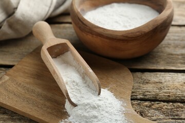 Baking powder in scoop and bowl on wooden table, closeup