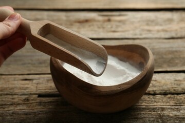 Woman taking baking powder with scoop from bowl at wooden table, closeup