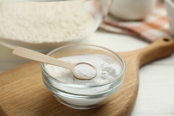 Fototapeta na wymiar Baking powder in bowl and spoon on white table, closeup