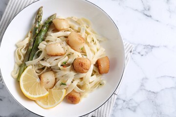 Delicious scallop pasta with asparagus and lemon on white marble table, top view. Space for text
