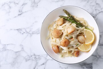 Delicious scallop pasta with asparagus and lemon on white marble table, top view. Space for text