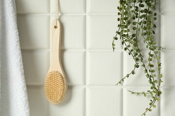 Bath accessories. Bamboo brush, terry towel and green plant on white tiled wall