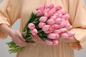 Woman holding bouquet of pink tulips on light grey background, closeup