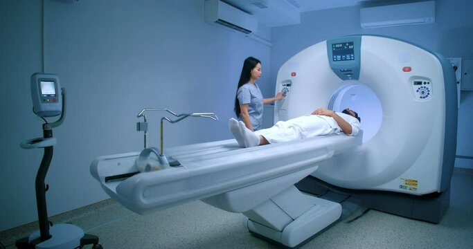 Asian doctor finishing magnetic resonance tomography. Patient lying at MRI capsule. MRI equipped cabinet. Undergoing tomography examination. Doctor asking how patient feel. CT scanner.