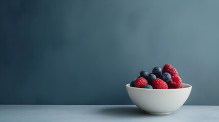 A white bowl is filled to the brim with a colorful assortment of ripe raspberries and plump blueberries - obrazy, fototapety, plakaty