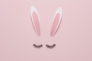 Minimal Easter concept. Bunny rabbit face made of paper bunny ears with eyelashes on pastel pink background. Flat lay.