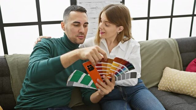 A man and woman examine paint swatches together in a cozy living room, discussing home decoration.