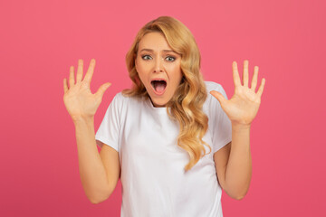 blonde woman raises hands in shocked gesture against pink backdrop