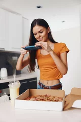 Deurstickers Woman taking picture with phone while holding pizza in front of her, capturing delicious moment © SHOTPRIME STUDIO