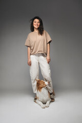 a young woman in light clothes stands with a dog on a gray background. Border collie dog breed.