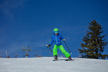 Skier kid glides on mountain under blue sky with chairlift