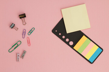 Office supplies top view with yellow sticky notepad on pink background.