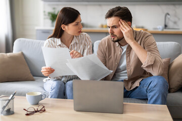 Worried couple reviewing finances with laptop and papers