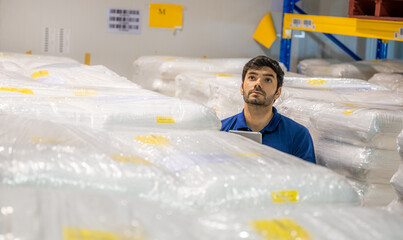 Male worker is checking stock or storage in a shelves of warehouse in rubber factory or...