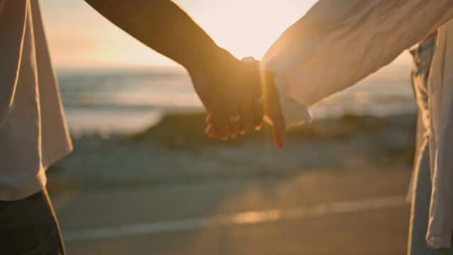 Dating lovers holding hands on sunrise sea beach close up. Couple touching arms
