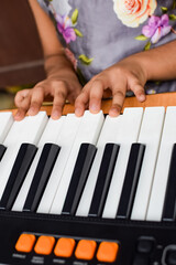 Fototapeta premium Asian cute girl playing the synthesizer or piano. Cute little kid learning how to play piano. Child's hands on the keyboard indoor.