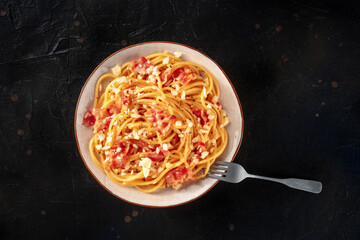 Carbonara pasta dish, traditional Italian spaghetti with pancetta and cheese, overhead flat lay shot with a fork on a black table - 752170922