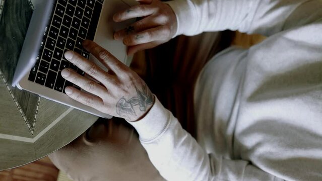 Close-up of the hands of a tattooed man working on a laptop
