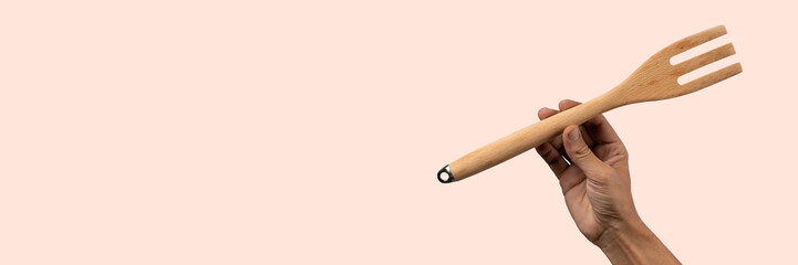 Hand holding wooden fork on light pink background, cutout