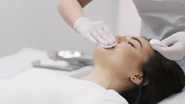 A female cosmetologist in white gloves prepares a syringe and lips of a young patient for cosmetic injections. Cosmetic injections, rejuvenation, cosmetologist services.