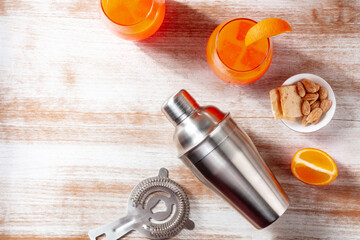 Orange cocktails and a shaker, overhead flat lay shot on a wooden background with a salty snack and...