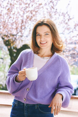 Spring portrait of happy beautiful woman drinking tea or coffee on balcony - 752174339