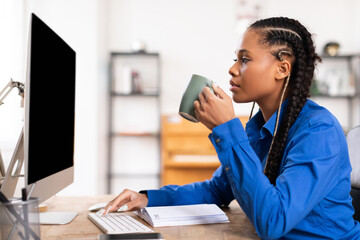 Focused black student lady with coffee at computer desk