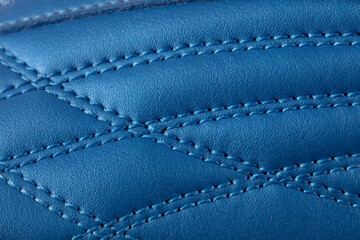 The macro texture of a blue leather sneaker with stitching. Part of the sports shoe is a close-up.