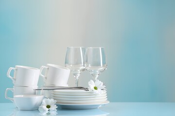 Set of many clean dishware, cutlery, flowers and glasses on light blue table. Space for text