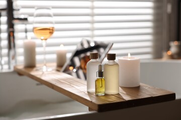 Wooden tray with tablet, wine, candles and toiletries on bathtub in bathroom, selective focus