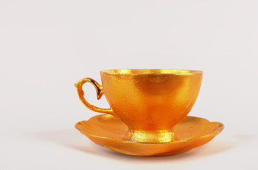 A golden tea cup with a saucer on a pink background.
