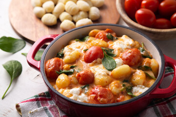 Close up of a casserole of gnocchi in creamy tomato sauce with baby spinach and melted mozzarella